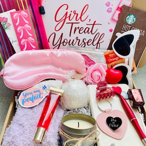 May include: A gift box filled with self-care items. Includes a pink satin eye mask, lip gloss, a candle, a bath bomb, a keychain that says "She is Fierce", a notebook, and a Starbucks hot cocoa packet. The box has the text "Girl, Treat Yourself".