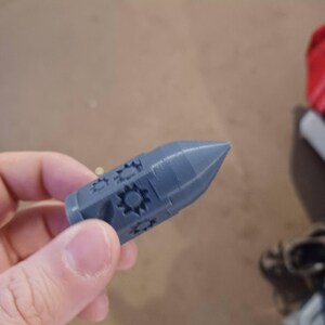 May include: A gray 3D printed rocket-shaped object with a detailed design of stars and circles.