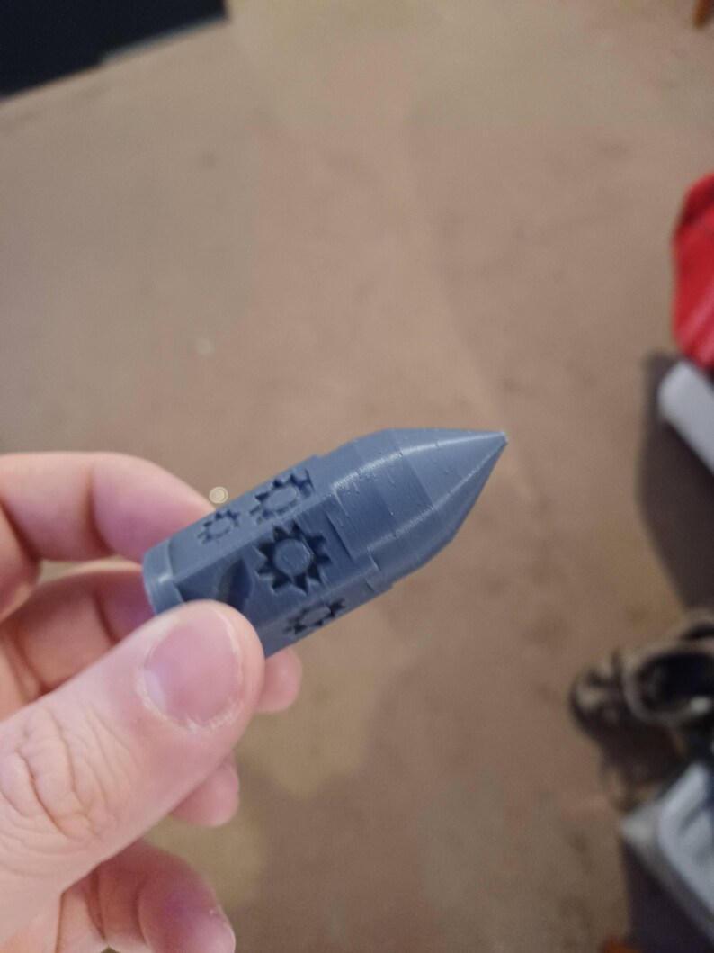 May include: A gray 3D printed rocket-shaped object with a detailed design of stars and circles.