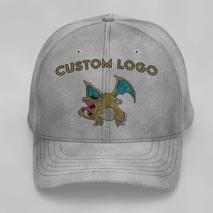 Puede incluir: Una gorra de béisbol gris con un logotipo personalizado que presenta un dragón de dibujos animados con alas azules y el texto "CUSTOM LOGO" en dorado.