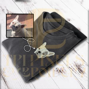 Puede incluir: Sudadera gris oscuro con un diseño de Bulldog Francés bordado. La sudadera tiene cuello redondo y está doblada. Una foto enmarcada de un Bulldog Francés está en la esquina superior izquierda. El diseño es en tonos grises, beige y marrón.