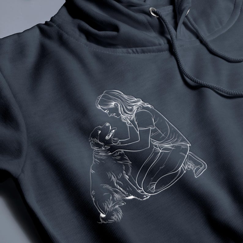 May include: A white line drawing of a person kneeling and petting a dog. The image is printed on a dark blue hoodie.