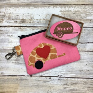 May include: Pink zippered pouch with a small wooden cutout of a camper trailer with the word "Happy" on it. The pouch has a small camper trailer design with a red heart on it.