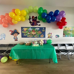 May include: A birthday party scene with a green tablecloth, balloons, and decorations. A rainbow arch of balloons hangs above the table. The wall features character posters and a cake with the number 5.
