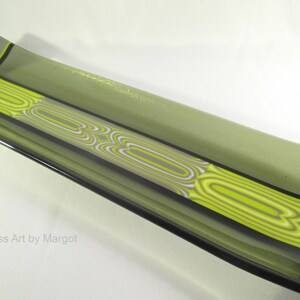 May include: A long, rectangular glass serving dish with a green base and a black and white striped design with yellow accents. The dish is slightly curved on the ends.