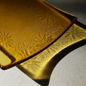 May include: Two amber glass plates with a floral design. The plates are stacked on top of each other, with the top plate slightly offset from the bottom plate.