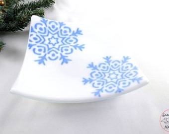 May include: White, square glass dish with two blue snowflake designs. The dish has a curved shape and is likely for decorative or serving purposes. The design is simple and elegant, suitable for winter or holiday decor.