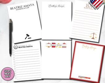 May include: A collection of white notepads with the name "Beatriz Amaya" printed on them. Some pads have lined pages, a gavel, or a scale of justice graphic. One notepad has a red border. A pen and an apple are also visible.
