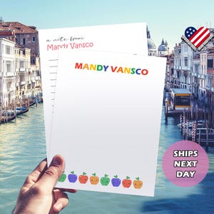 Pu&ograve; includere: Un blocco note bianco con un bordo di mele arcobaleno. Il blocco note ha il testo "a note from Mandy VanscO" e "MANDY VANSCO" stampato su di esso.