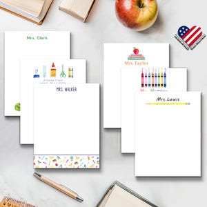 May include: A collection of white personalized stationery notepads featuring various school-themed watercolor illustrations including crayons, books, apples, and school supplies, with printed names such as Mrs. Clark, Mrs. Walker, Mrs. Taylor, and Mrs. Lewis.