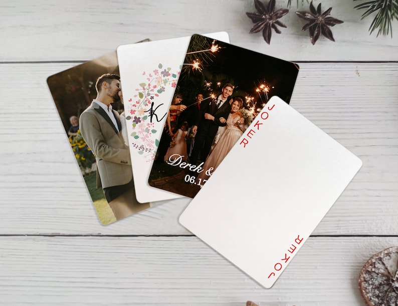 K&ouml;nnte beinhalten: Vier Hochzeitseinladungskarten mit unterschiedlichen Designs. Eine Karte zeigt einen Blumenkranz mit dem Buchstaben K in der Mitte. Eine andere Karte zeigt ein Foto eines Paares, das Wunderkerzen h&auml;lt. Die dritte Karte zeigt ein Foto eines Paares in Abendgarderobe. Die vierte Karte ist leer mit dem Wort "JOKER" in rot oben und unten gedruckt.