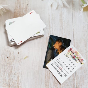 K&ouml;nnte beinhalten: Eine Save-the-Date-Karte f&uuml;r eine Hochzeit mit einem floralen Design und einem Foto eines Paares. Die Karte enth&auml;lt einen Kalender mit dem hervorgehobenen Datum 21. Juli 2028.