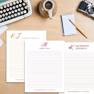 May include: Three white lined notepads with different monogrammed designs. The first notepad has the initials "KJ" in orange with the name "Kennedy Jessica" below. The second notepad has the initial "K" in pink with the name "Kennedy Jessica" below. The third notepad has the initial "K" in red with the name "Kennedy Jessica" below.