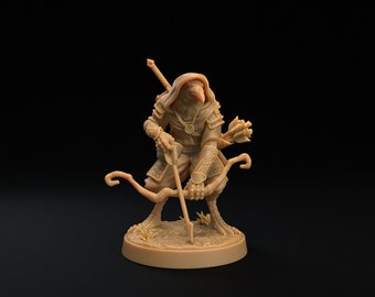 Puede incluir: Una figurita miniatura marrón de un humanoide con cabeza de pájaro, que lleva una capa con capucha y sostiene un arco y una flecha.