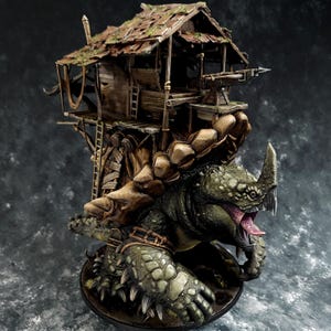 Puede incluir: Un modelo en miniatura de una gran criatura reptiliana verde con un cuerno de rinoceronte y una boca abierta. La criatura lleva una pequeña casa de madera destartalada en su espalda.