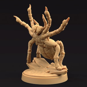 May include: A beige, detailed figurine of a large spider with multiple legs and sharp claws. The spider is posed on a small rock formation, mounted on a circular base. The figurine has a textured, furry appearance.