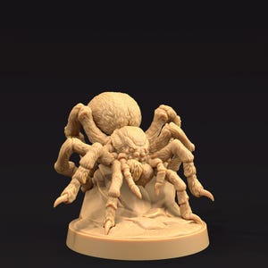 May include: A tan-colored, detailed miniature spider figurine. The spider has a large, hairy abdomen and multiple legs, posed on a rocky base. The figurine is likely made of resin or a similar material, and is designed for tabletop gaming or display.
