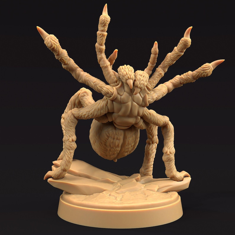 May include: A tan-colored, detailed figurine of a large spider with multiple legs and a bulbous abdomen. The spider is posed on a small, rocky base, and the overall design suggests a fantasy or tabletop gaming theme.