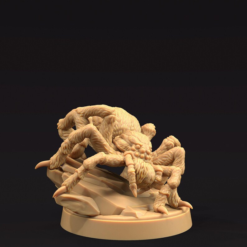May include: A detailed, beige-colored miniature of a large spider, posed on a small rock formation. The spider has multiple legs, a hairy body, and a menacing expression. The miniature is set against a dark background.