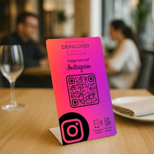 Könnte beinhalten: Ein pink-lila Farbverlauf-Tischaufsteller mit Instagram-Logo und QR-Code. Der Text "DEIN LOGO" und "Folge uns auf Instagram" sind abgebildet. Der Aufsteller steht auf einem Holztisch.