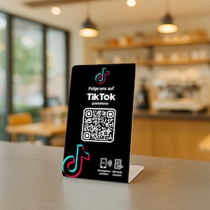 Könnte beinhalten: Ein schwarzes Schild mit einem TikTok QR-Code. Das TikTok-Logo befindet sich oben links und unten links. Der Text "Folge uns auf TikTok @deinName" und Symbole für NFC und QR-Code-Scannen.