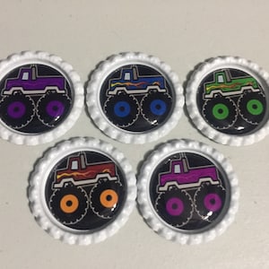 May include: Five monster truck bottle cap charms with different colored trucks and wheels. The trucks are black with flames and the wheels are purple, blue, green, orange, and pink.