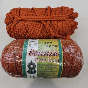 May include: A bundle of burnt orange craft cord and a wrapped spool of the same cord. The label reads Bonnie Craft Cord, 6 mm, 100 yd / 90 m, and features illustrations of a dreamcatcher. The cord is a thick, braided fiber material.