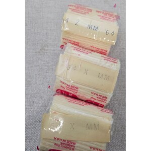 May include: Three rectangular packages of off-white yarn, each wrapped in clear plastic with a paper label. The labels feature red text reading MOTHPROOF, NON-ALLERGENIC, MADE IN U.S.A., and include specific size markings like 4 2 MM 64.