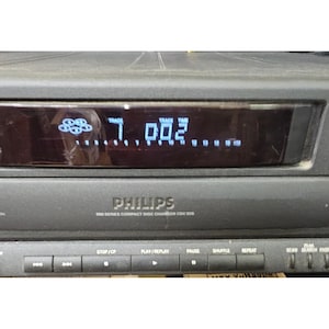 May include: A black Philips 900 Series Compact Disc Changer CDC 926 with a digital display showing track information. The front panel features control buttons for stop, play, replay, pause, shuffle, repeat, and scan functions in a horizontal row.