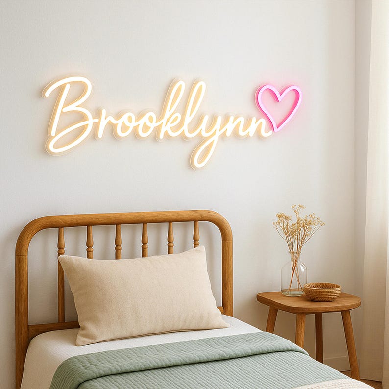 Puede incluir: Una cabecera de cama de madera blanca con un letrero de ne&oacute;n blanco que dice "Brooklynn" con un coraz&oacute;n de ne&oacute;n rosa. La cama tiene una almohada blanca y una colcha verde.