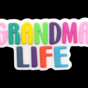 May include: A colorful, whimsical charm with the words "GRANDMA LIFE" in a variety of bright colors. The letters are raised and outlined in white, set against a black background. A fun accessory.