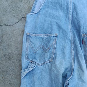 Op de afbeelding: Lichtblauwe denim overall met een klassiek ontwerp. Kenmerken zijn een borstzak aan de voorkant, zijzakken en een achterzak met een kenmerkend gestikt ontwerp. De overall is gemaakt van duurzaam denim materiaal.