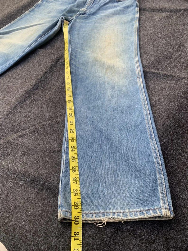 Puede incluir: Vaqueros de mezclilla azul claro con pernera acampanada, medidos con una cinta m&eacute;trica amarilla. Los vaqueros miden aproximadamente 79 cm de largo.