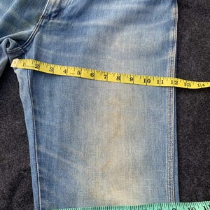 Puede incluir: Vaqueros de mezclilla azul claro con una cinta m&eacute;trica amarilla que muestra una medida de 33 cm. Una cinta m&eacute;trica verde muestra una medida de 25 cm. Los vaqueros tienen un aspecto descolorido con parches m&aacute;s claros.