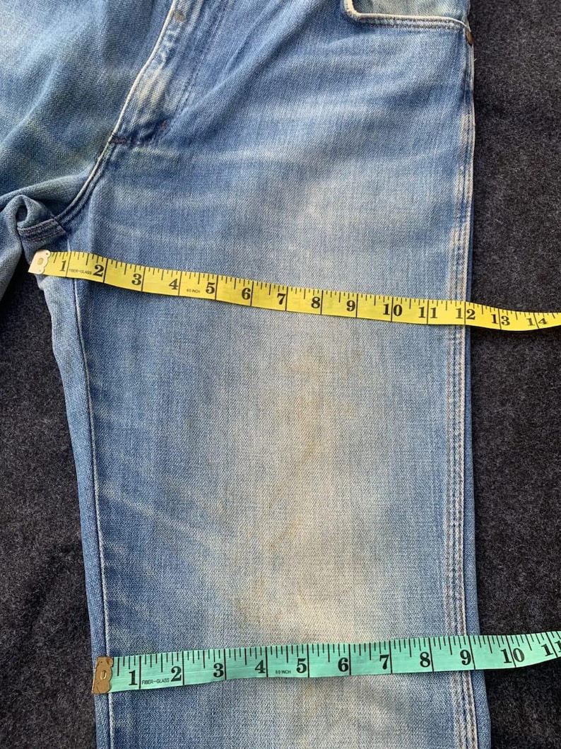 Puede incluir: Vaqueros de mezclilla azul claro con una cinta m&eacute;trica amarilla que muestra una medida de 33 cm. Una cinta m&eacute;trica verde muestra una medida de 25 cm. Los vaqueros tienen un aspecto descolorido con parches m&aacute;s claros.