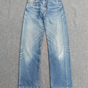 Puede incluir: Unos pantalones vaqueros de mezclilla azul con un lavado desgastado, diseño clásico de cinco bolsillos con remaches metálicos, cierre de botones y perneras rectas con dobladillos deshilachados, mostrando patrones de desgaste y arrugas naturales.