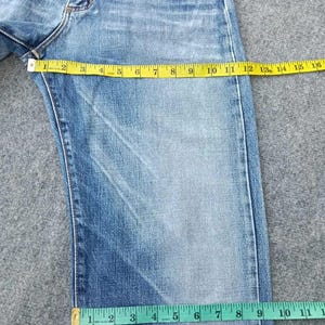 Pu&ograve; includere: Jeans di denim blu chiaro sbiadito con un metro a nastro giallo che mostra una misurazione della vita di 40,6 cm. I jeans hanno un classico design a cinque tasche. La larghezza della gamba &egrave; misurata a 27,9 cm.