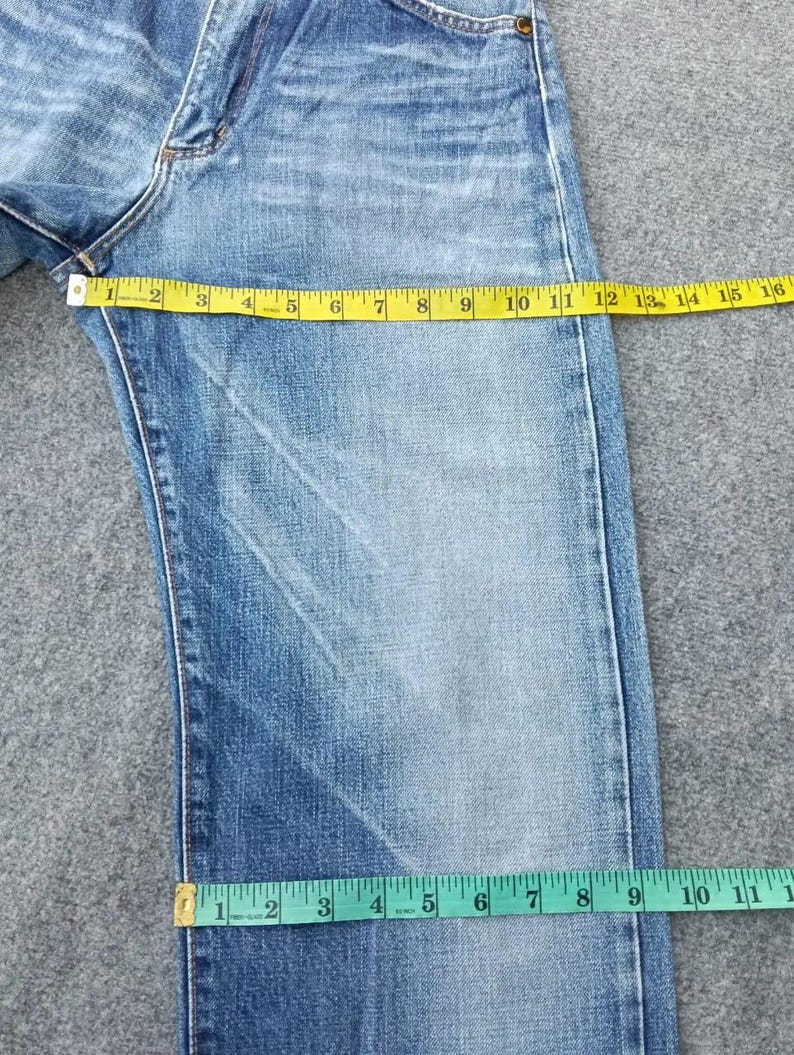 Pu&ograve; includere: Jeans di denim blu chiaro sbiadito con un metro a nastro giallo che mostra una misurazione della vita di 40,6 cm. I jeans hanno un classico design a cinque tasche. La larghezza della gamba &egrave; misurata a 27,9 cm.