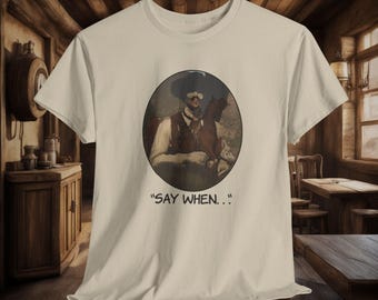 Può includere: Una t-shirt beige con un'immagine circolare di un uomo con un cappello che cavalca un cavallo. Il testo "SAY WHEN..." è stampato sotto l'immagine.