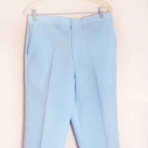 May include: Light blue trousers hanging on a white hanger. The pants have a classic design with a button and zipper closure, belt loops, and front pockets. The fabric appears to be a lightweight material, suitable for warmer weather.