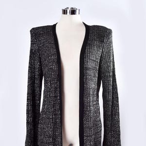 May include: A long black cardigan with silver glitter throughout. The cardigan has a V-neck and long sleeves.