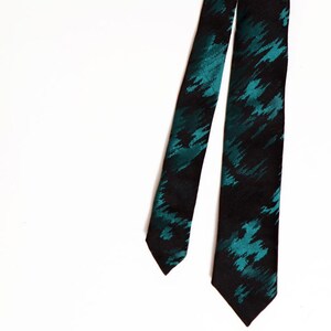 May include: A black necktie with a teal abstract pattern. The tie is made of a smooth fabric and is displayed against a white background. The tie is a classic accessory for formal or business attire.