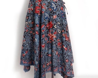 Può includere: Una gonna a portafoglio con base blu scuro e un motivo denso e complesso di fiori e foglie nei toni del rosso, azzurro e crema. La gonna presenta un orlo asimmetrico e una chiusura a laccio in vita, esposta su un manichino.