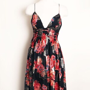 May include: A black maxi dress with a deep V-neck and spaghetti straps. The dress features a floral pattern in red, pink, and gold metallic accents. The dress is displayed on a white mannequin.