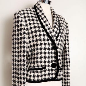 Può includere: Un blazer a quadri pied-de-poule in bianco e nero con finiture e bottoni in velluto nero. La giacca, esposta su un manichino, presenta un design classico e una vestibilità su misura. Ha un revers a lancia e una chiusura monopetto.