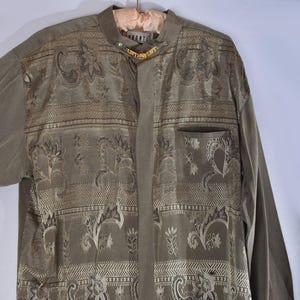 May include: A long-sleeved, green button-up shirt with a paisley pattern. The shirt has a mandarin collar and a gold chain with the word "Pronto" on it.