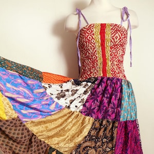 Könnte beinhalten: Ein Patchwork-Maxikleid auf einer Schaufensterpuppe. Das Oberteil ist rot mit einem geometrischen Muster und gelben und roten Streifen. Der Rock besteht aus verschiedenen bunten Stoffen, darunter Blau, Lila, Gold und Braun, mit Paisley- und Blumenmustern.