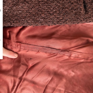 May include: Close-up of the lining of a brown jacket. The lining is a reddish-brown color and has a small hole in it. The text "Liner has normal small flaws from wear & age. No real damage or big stains slight darkening here n there small hole" is visible in the image.