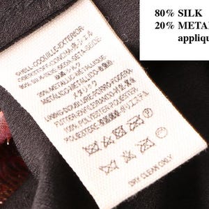May include: Close-up of a clothing tag with text in multiple languages. The tag indicates the garment is 80% silk and 20% metallic applique. The care instructions include dry clean only.