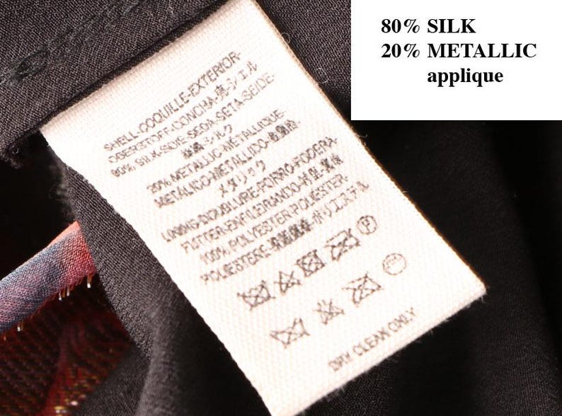 May include: Close-up of a clothing tag with text in multiple languages. The tag indicates the garment is 80% silk and 20% metallic applique. The care instructions include dry clean only.
